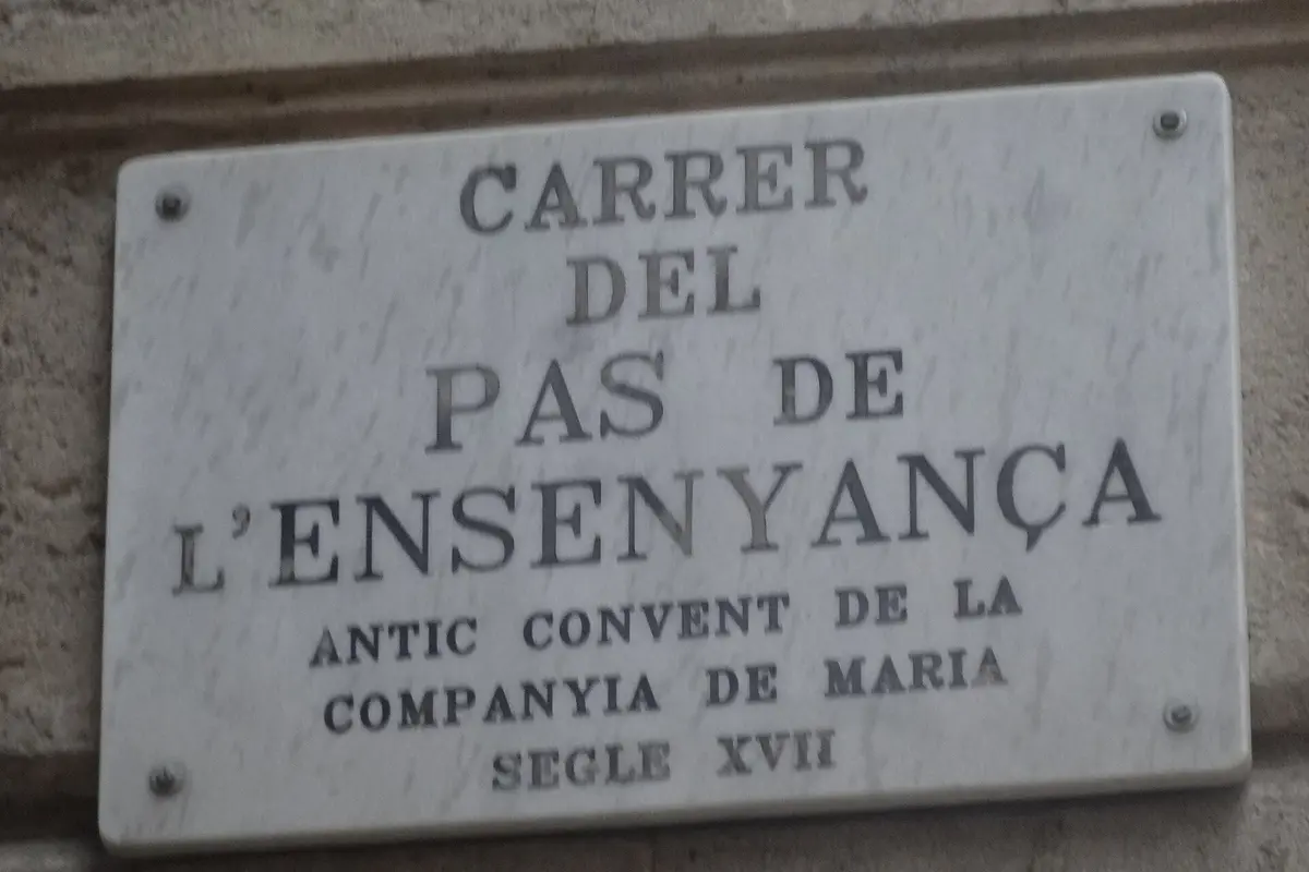 A marble street plaque reading Carrer del Pas de l'Ensenyança, antic convent de la Companyia de Maria, segle XVII
